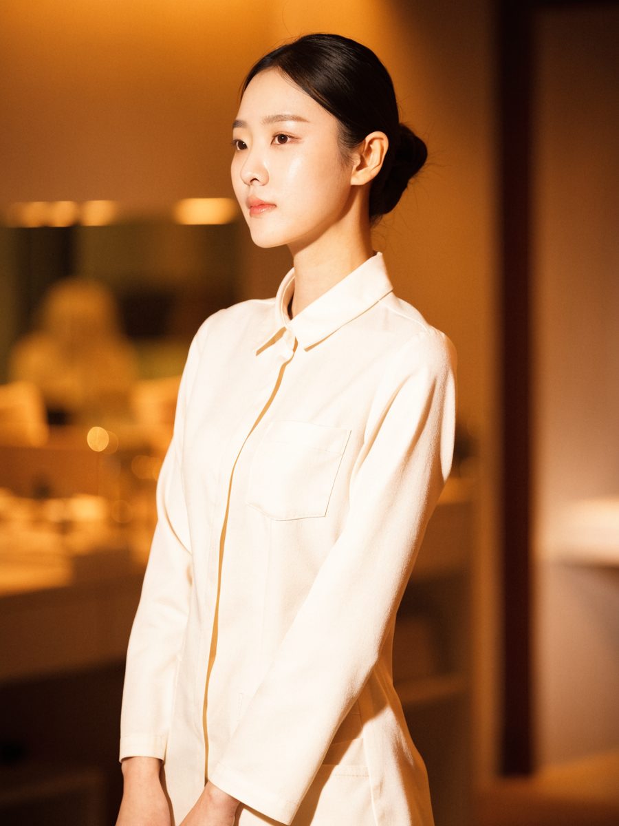 아이보리 유니폼을 입고 트리트먼트룸에 서 있는 담당 테라피스트